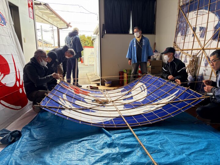 倉庫の中での組み立て作業。竹骨に糸を張り、結びを整える場面。