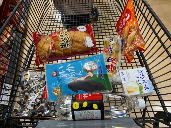 カラオケ前にスーパーで購入したパンやチーズや菓子と飲料が入った買い物カゴ