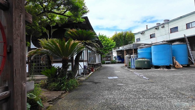 万大醸造の敷地内に並ぶ青いカバーで保護された酒造用タンクと風格ある木造建築