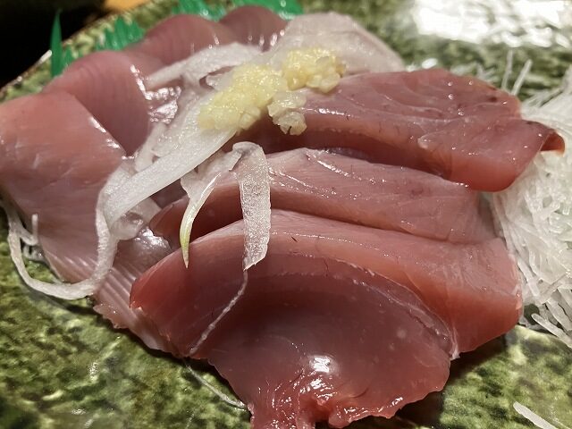 玉ねぎとおろし生姜を添えた厚切りのカツオの刺身
