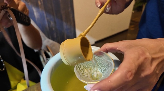 萬寿鏡の甕覗を小さなひしゃくですくってガラスの酒器へ注ぐ様子