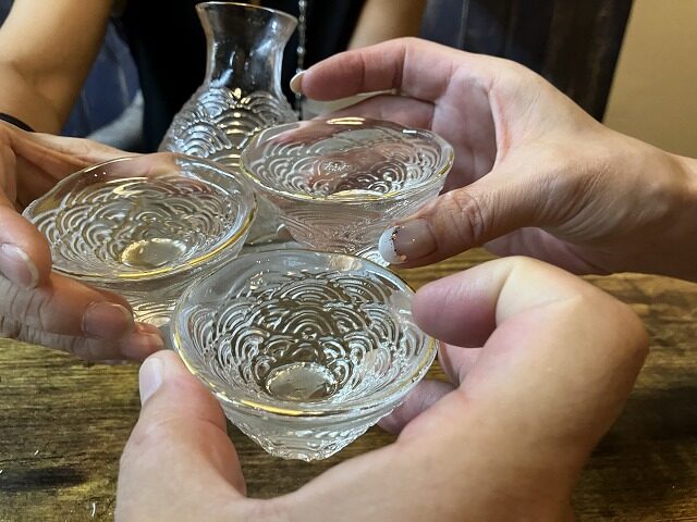 波紋模様のガラス酒器に注いだ萬寿鏡の甕覗で乾杯する様子