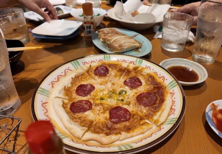 サラミやコーンがたっぷり乗った焼きたてピザと奥に並ぶ餃子