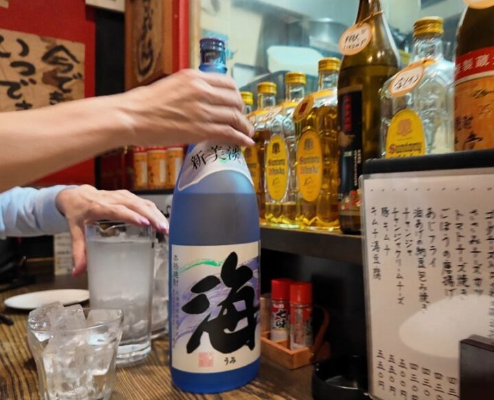 カウンターに置かれた本格芋焼酎「海」の青い一升瓶と氷の入ったグラス