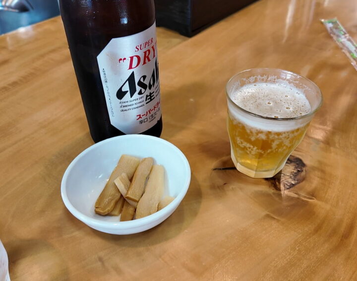 カウンターに置かれたアサヒスーパードライの瓶ビールと小皿に盛られたメンマのお通し