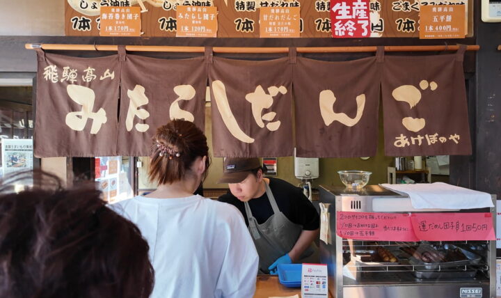 飛騨高山みたらしだんごと染め抜かれた茶色いのれんと注文カウンター