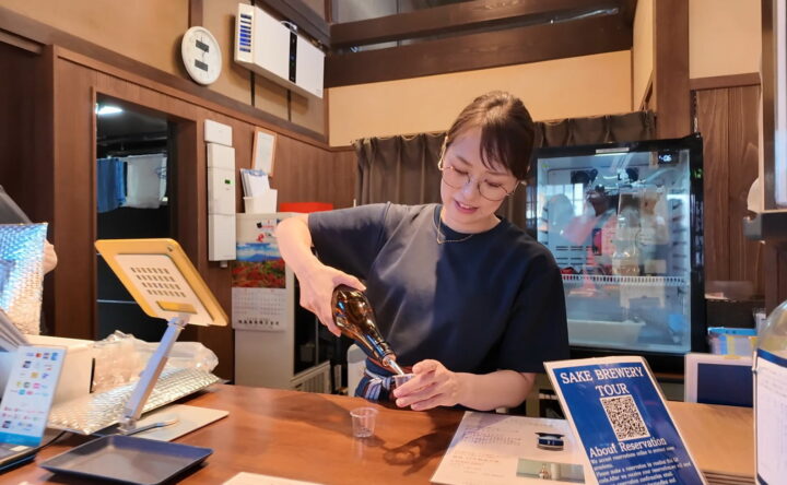 平田酒造場のカウンターでスタッフが笑顔でお酒をカップに注いでくれる様子