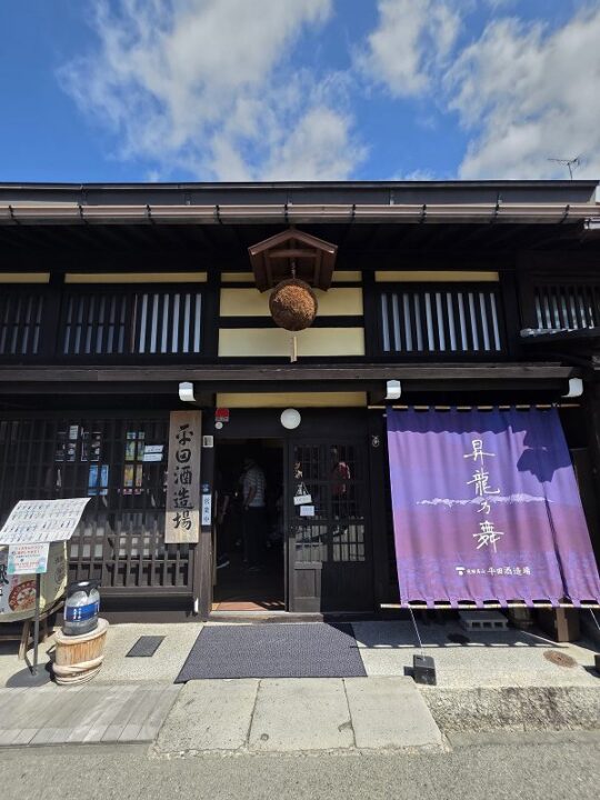 青空に映える平田酒造場の黒格子町家と屋根付き杉玉、紫の昇龍乃舞暖簾