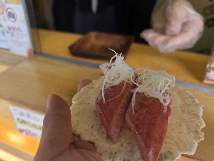 注文口のカウンター越しに手渡されたあおさ海苔せんべい上の飛騨牛トロさし握り